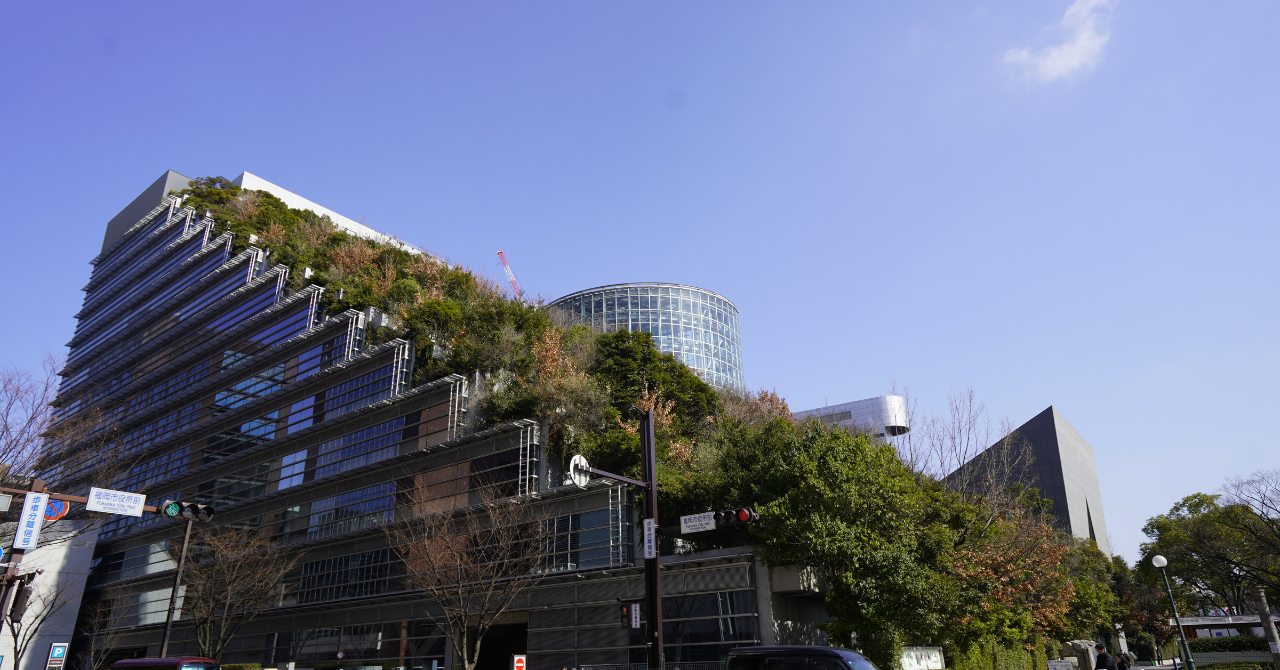 街路から見上げた、緑に覆われたアクロス福岡のステップガーデンとガラス建築