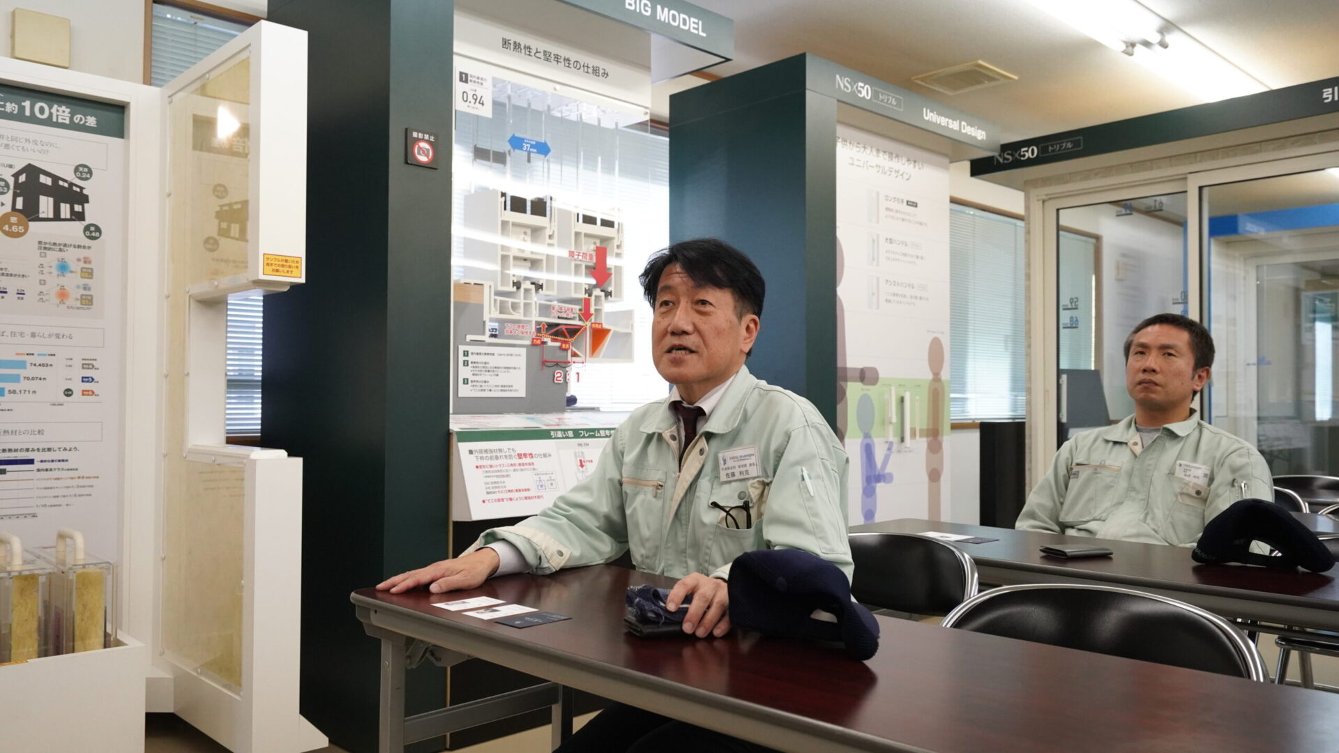 断熱性能や構造を示す展示模型の前で説明を受ける工場見学の様子