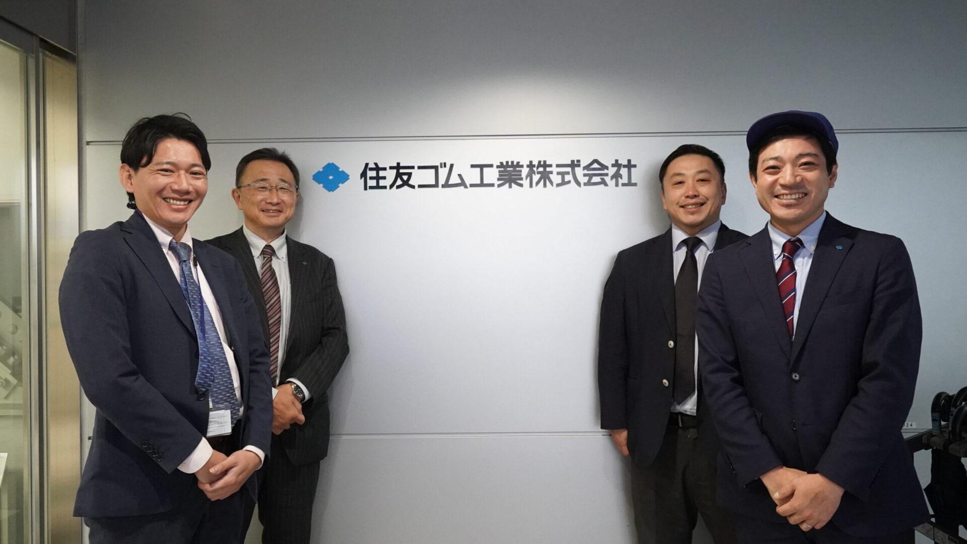 住友ゴム工業の社員と健康住宅の取材メンバーが、企業ロゴの前で並ぶ取材記念の集合写真