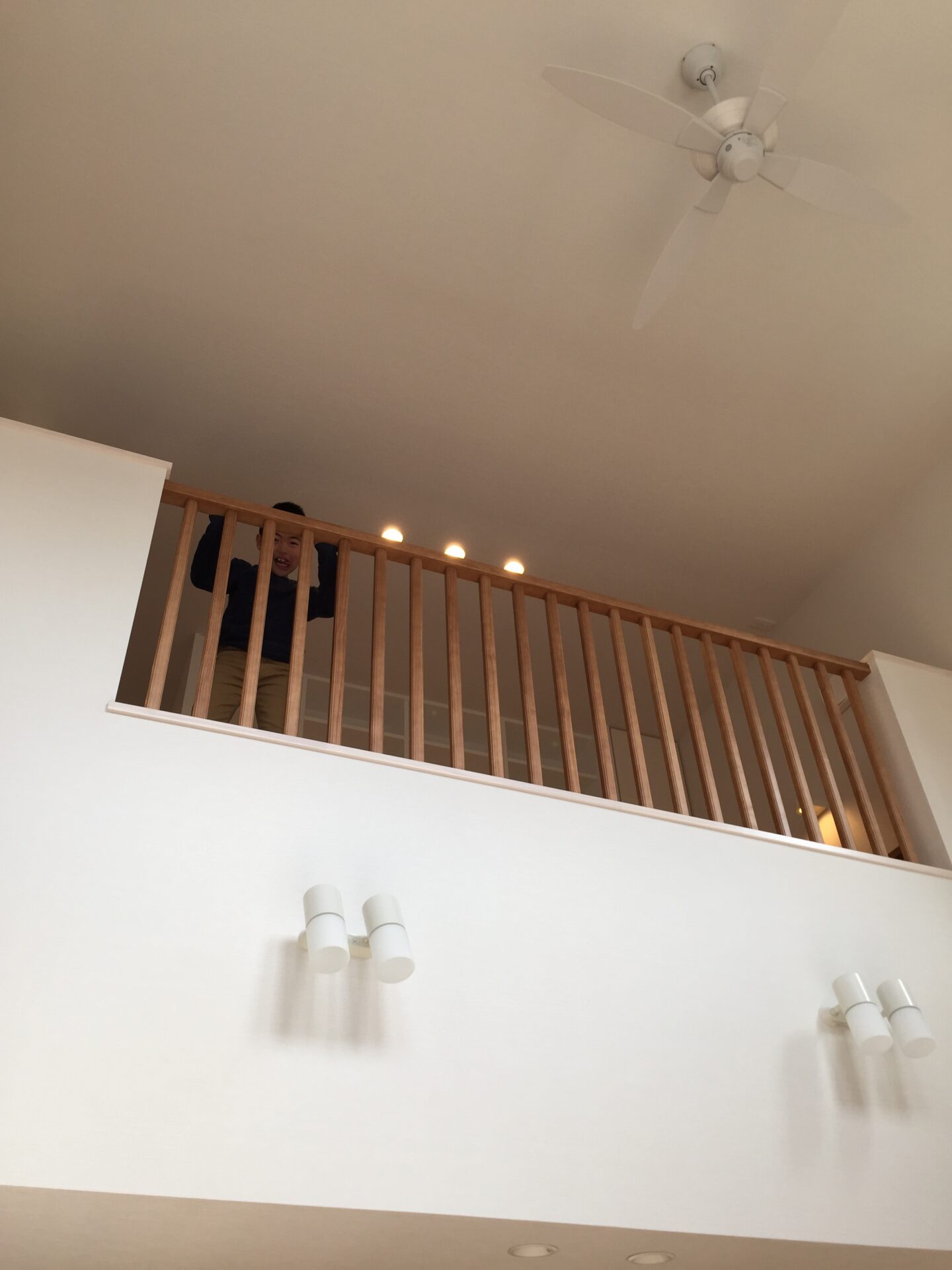 吹き抜けのあるリビングで、2階の手すり越しに子どもが顔を出している様子