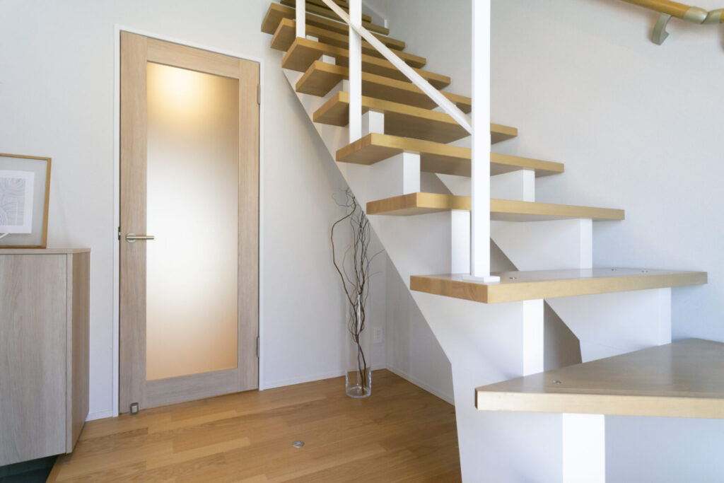 木の踏み板を使ったスケルトン階段と室内ドアが並ぶ明るいホール空間