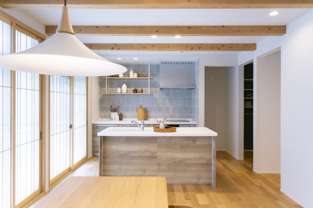 ペンダント照明越しに見た対面キッチンと木の梁のある天井