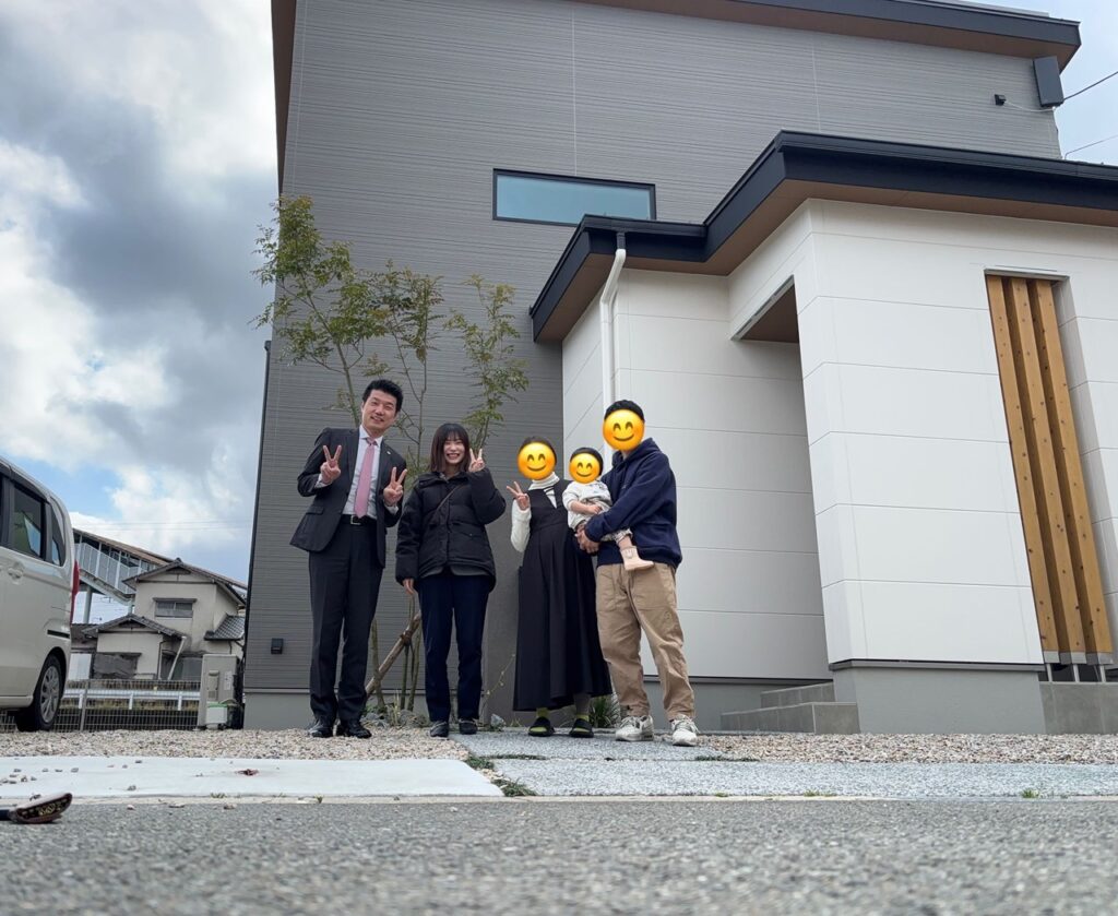 新築住宅の前で、担当スタッフと施主家族が並んで立ち、笑顔で記念撮影している様子