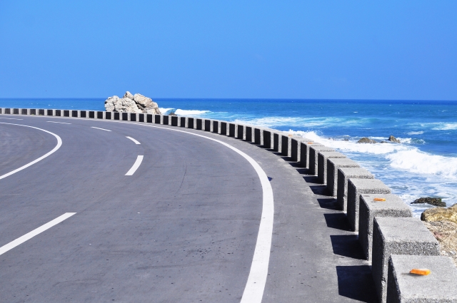 海岸沿いを緩やかにカーブする舗装道路と、その脇に広がる青く澄んだ夏の海