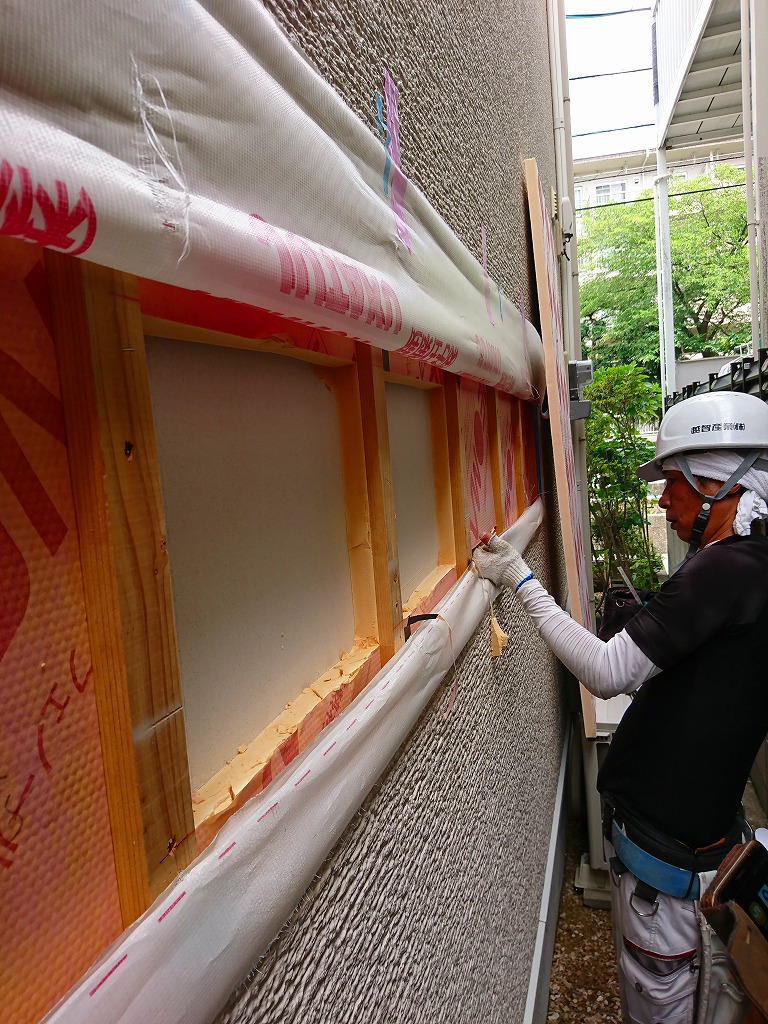 建物外壁の断熱材確認作業を見守る関係者たちと、開口部の防水シートを確認する職人