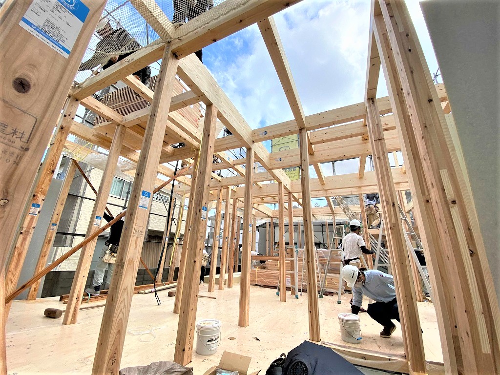 木造住宅の1階部分の柱が立ち並ぶ中で作業を進める複数の職人たち