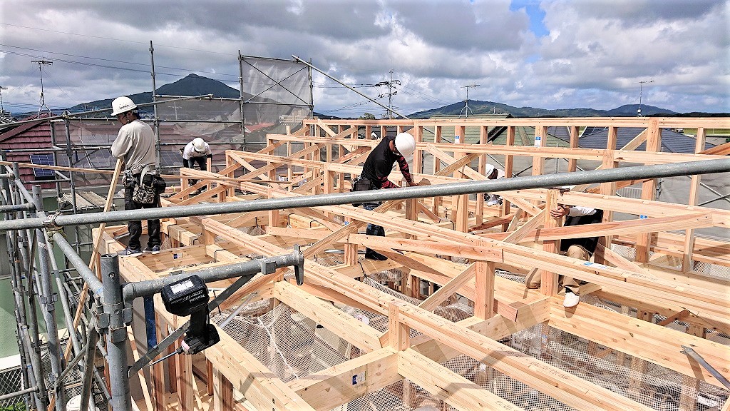 足場の組まれた現場で木造住宅の屋根部分を組み上げる複数の大工たち