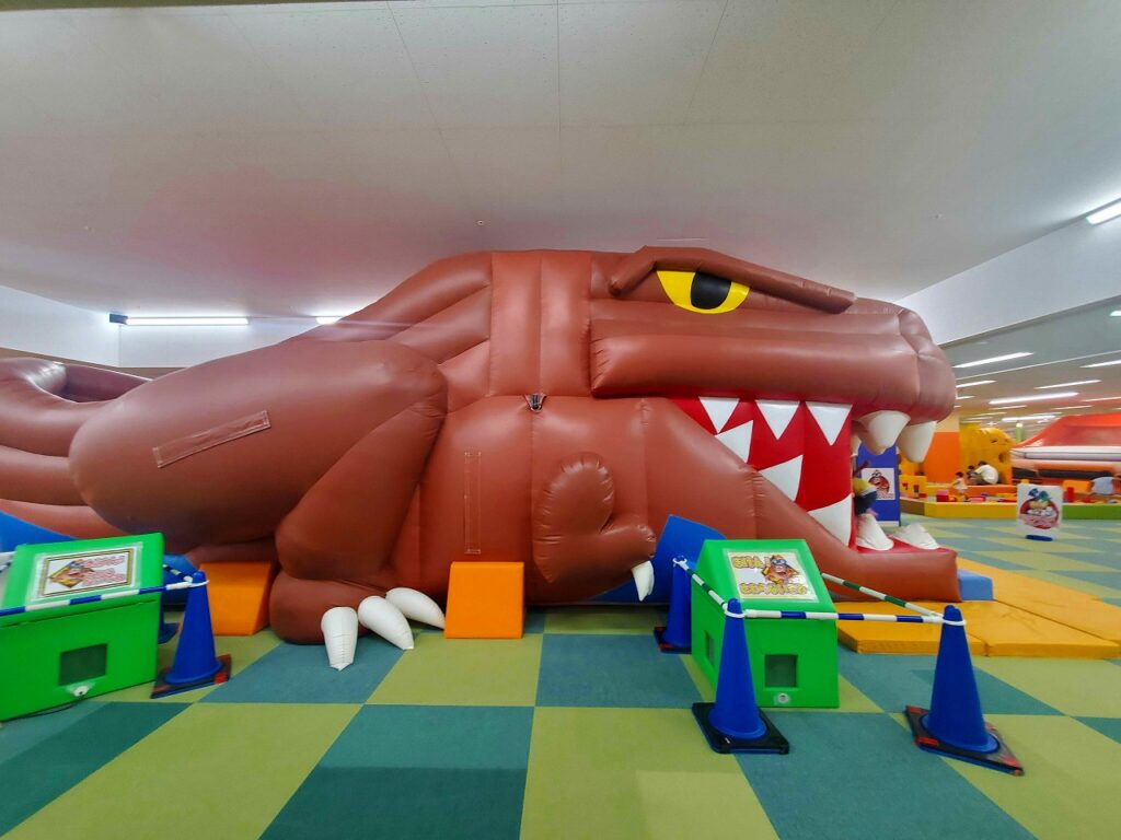 室内に設置された巨大な茶色の恐竜型ふわふわ遊具と、その出入口付近の様