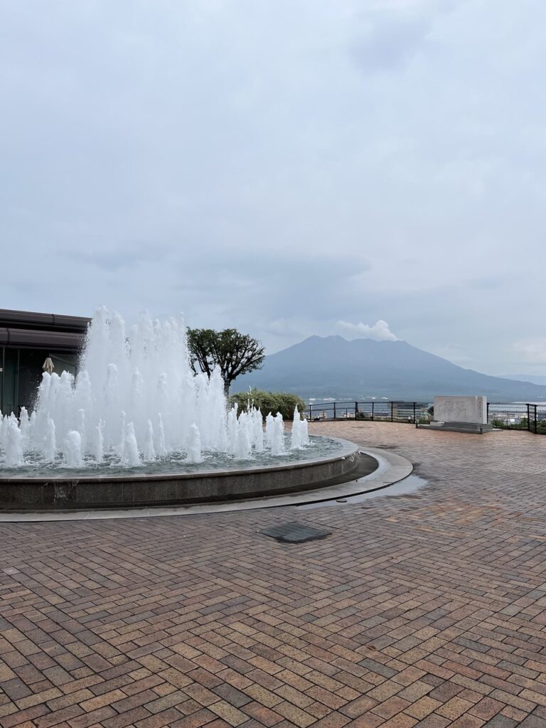 噴水越しに桜島を望む城山ホテル近くの展望スポット。曇り空ながらも雄大な風景