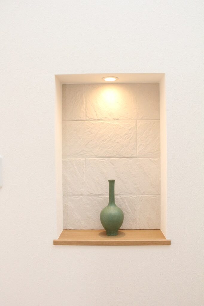 照明付きのニッチに飾られたシンプルなグリーンの一輪挿しの花瓶