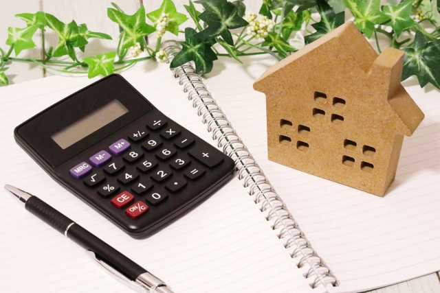 住宅ローンに関するイメージ。ノートの上に置かれた電卓とペン、そして家の形をした木製の模型