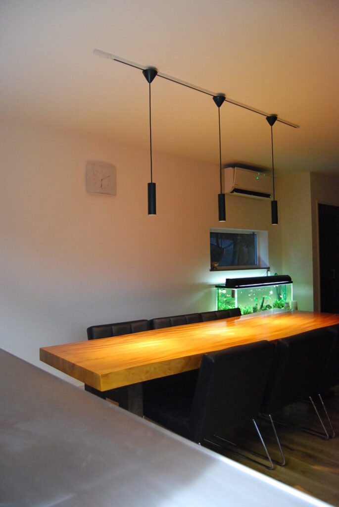 無垢材のダイニングテーブルと水槽が照明に照らされ、温かみのある空間を演出するリビングダイニング