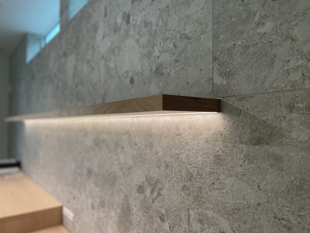 石調タイルの壁に取り付けられた間接照明付きの木製棚