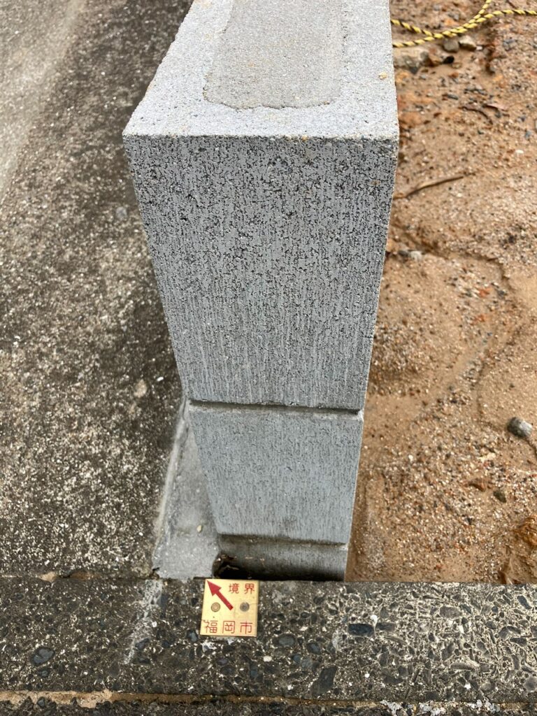 境界ライン上に建てられたブロック塀とその手前に設置された福岡市の境界プレート