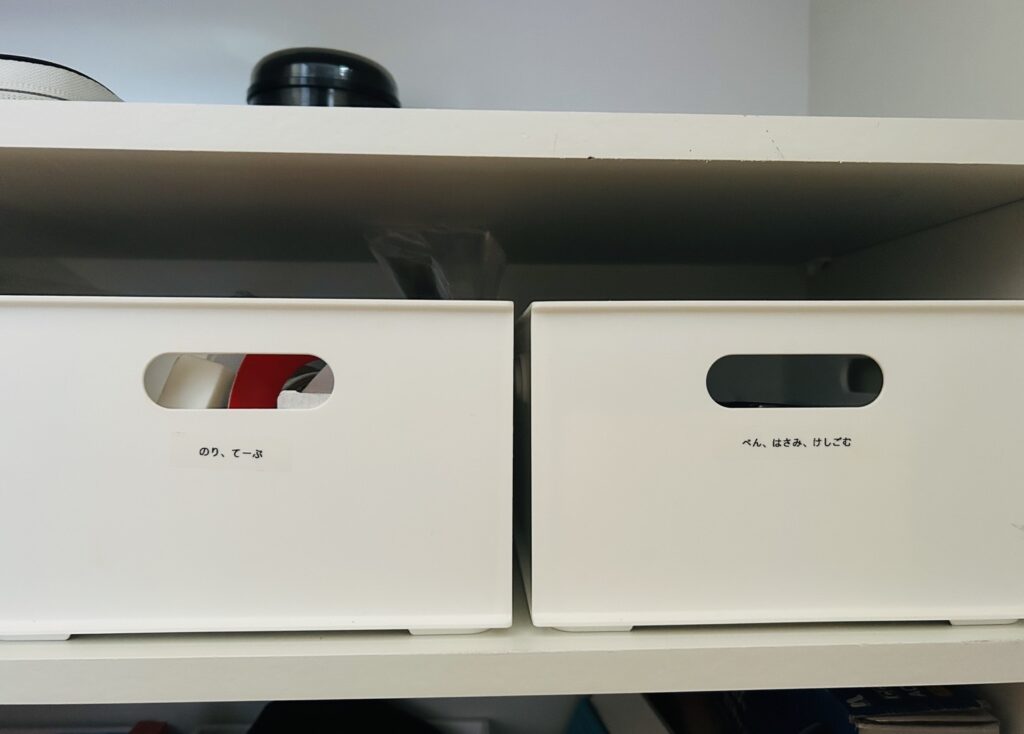 中身が見えない白い収納ボックスにラベルを貼り、文房具や日用品を分かりやすく整理している収納の工夫