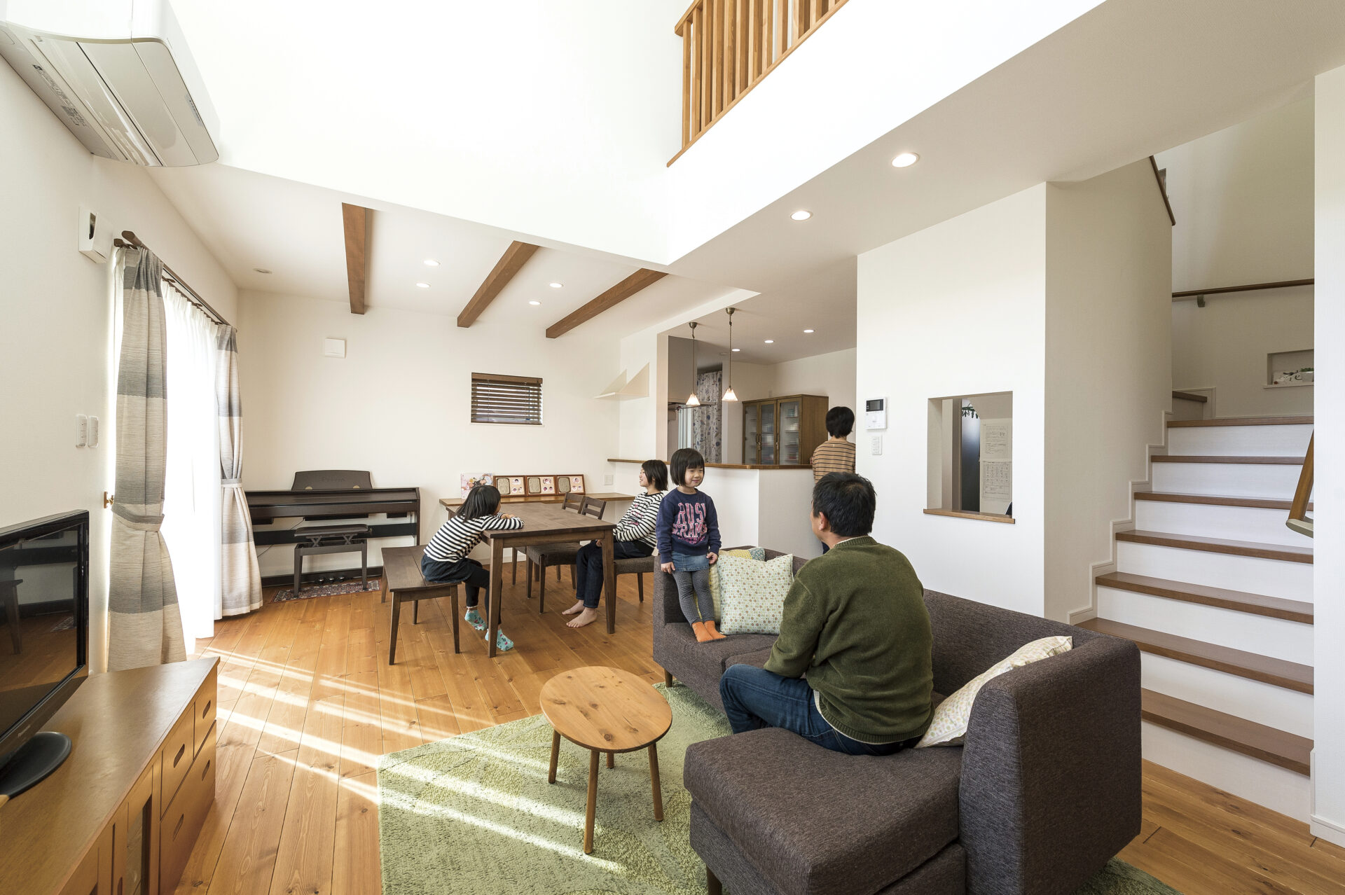 吹き抜けのある開放的なリビングでくつろぐK様ご家族。温かい木の床と自然光が心地よい空間