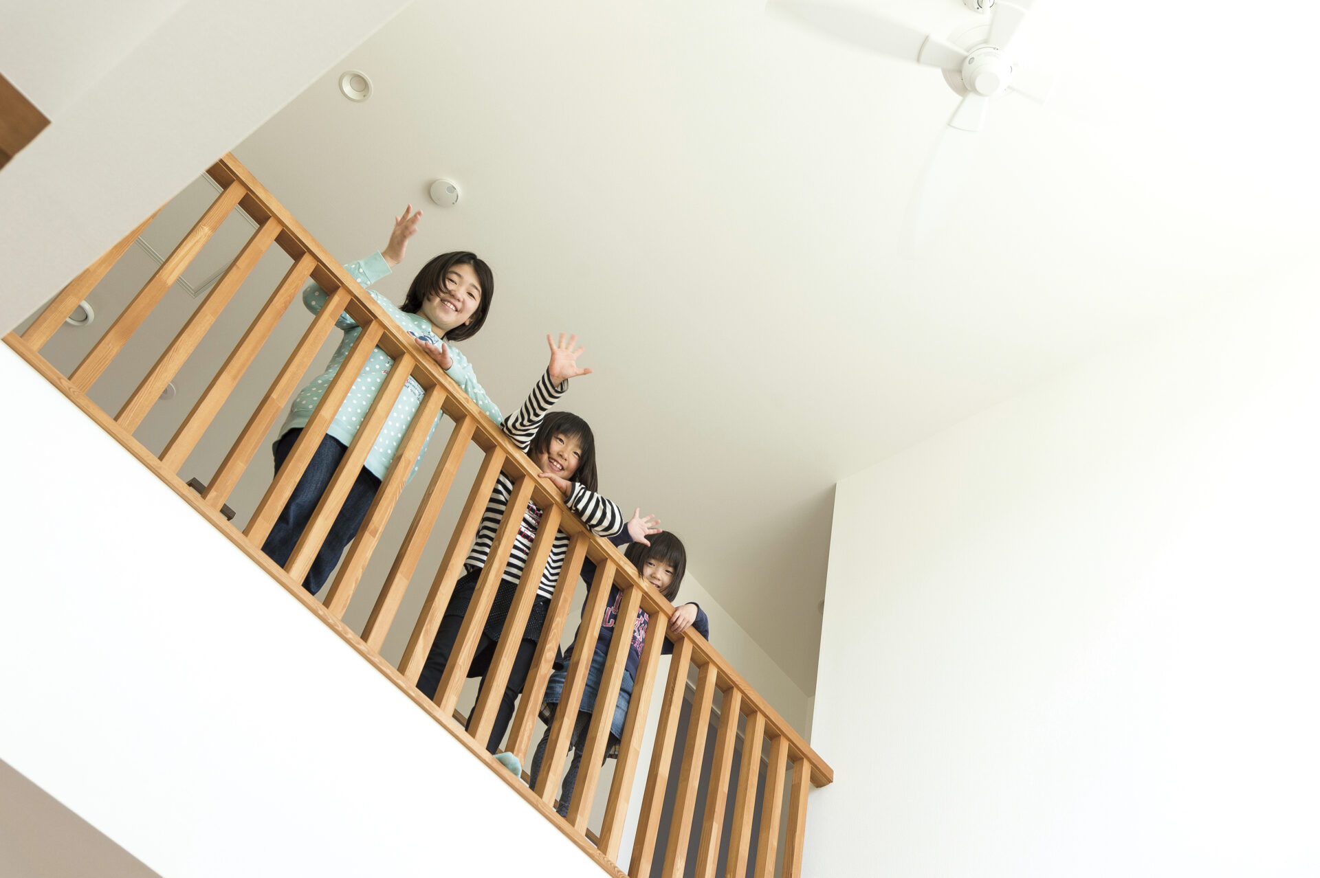 吹き抜けの手すりから笑顔で手を振る三姉妹。上下階のつながりと家族の一体感を感じるシーン